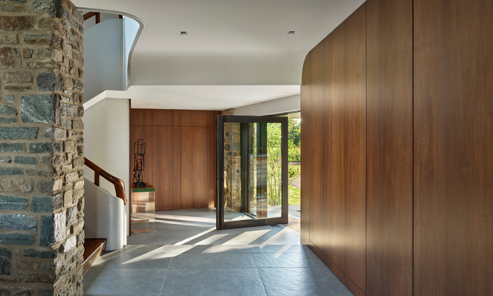Esempio di un ingresso o corridoio moderno con pareti marroni, pavimento in gres porcellanato, una porta a pivot, una porta in vetro, pavimento grigio e pareti in legno