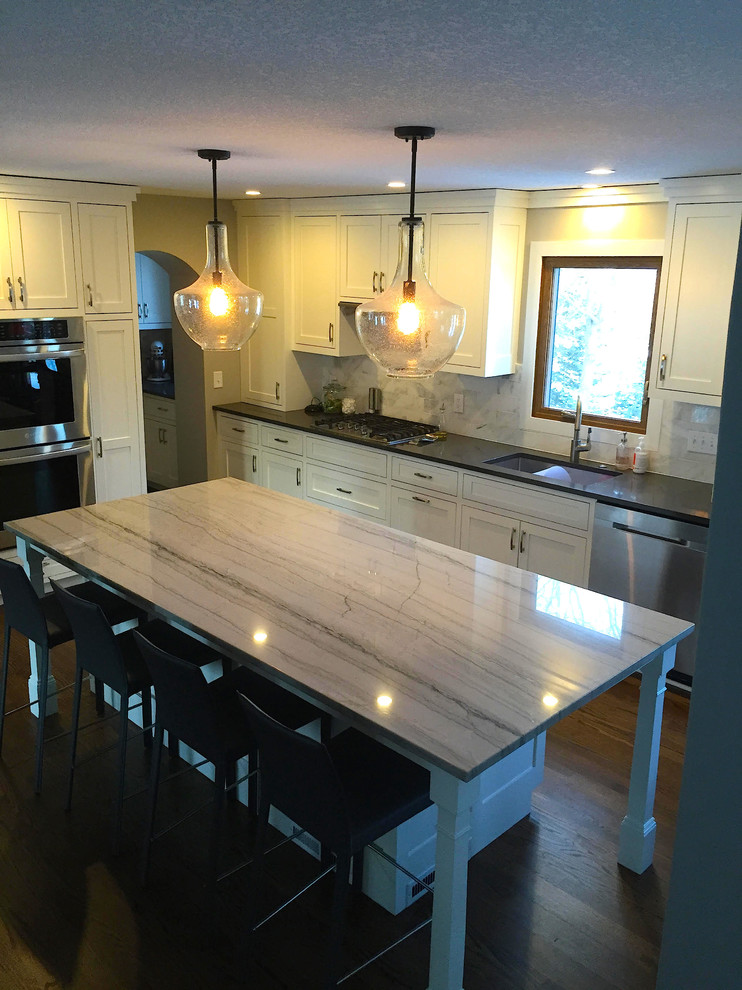 Inspiration for a large transitional dark wood floor and brown floor kitchen remodel in Minneapolis with an undermount sink, shaker cabinets, white cabinets, quartzite countertops, gray backsplash, stone tile backsplash, stainless steel appliances and an island