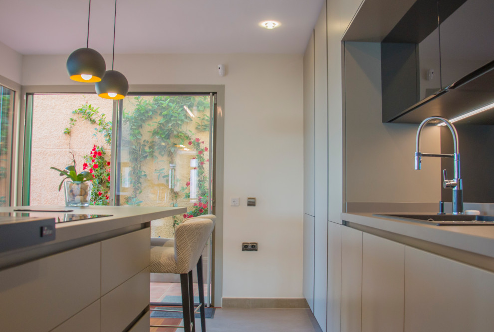 This is an example of a large modern single-wall open plan kitchen in Malaga with a farmhouse sink, grey cabinets, black splashback, glass tile splashback, black appliances, medium hardwood floors, with island and orange floor.
