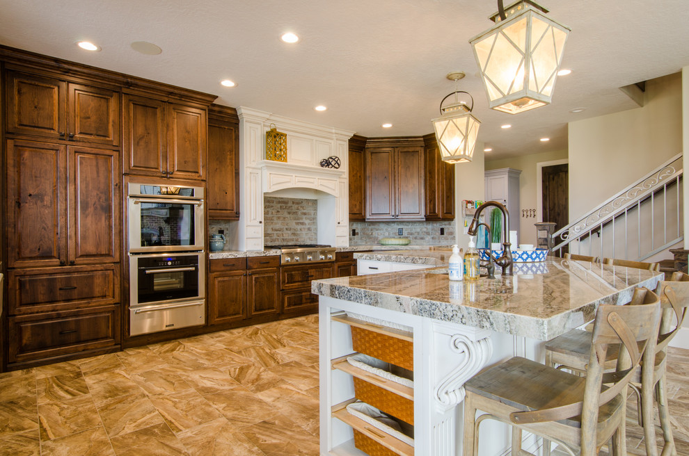 Large arts and crafts galley eat-in kitchen in Salt Lake City with a farmhouse sink, raised-panel cabinets, medium wood cabinets, granite benchtops, beige splashback, stone tile splashback, stainless steel appliances, ceramic floors and with island.