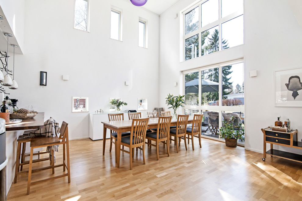 Contemporary open plan dining in Stockholm with white walls, light hardwood floors, no fireplace and brown floor.
