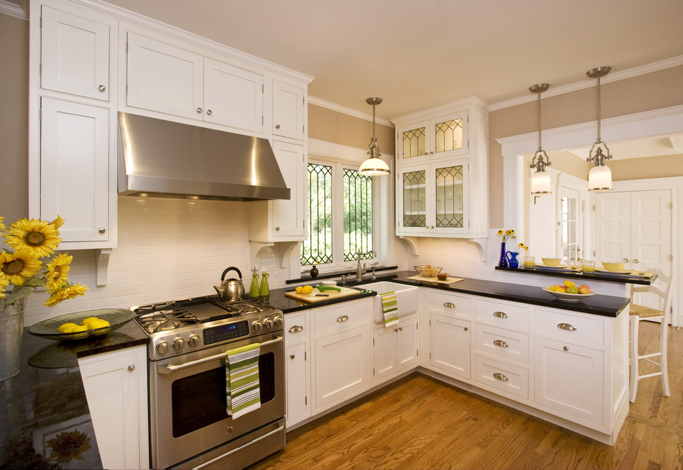 This is an example of a mid-sized traditional u-shaped separate kitchen in New York with beaded inset cabinets, panelled appliances, a farmhouse sink, granite benchtops, white splashback, ceramic splashback, a peninsula, white cabinets and medium hardwood floors.