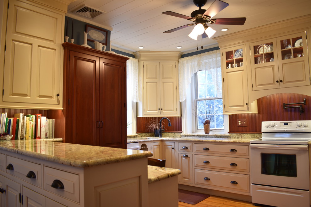 Photo of a mid-sized country u-shaped eat-in kitchen in Other with an undermount sink, raised-panel cabinets, beige cabinets, granite benchtops, brown splashback, timber splashback, white appliances, light hardwood floors, a peninsula, brown floor and multi-coloured benchtop.