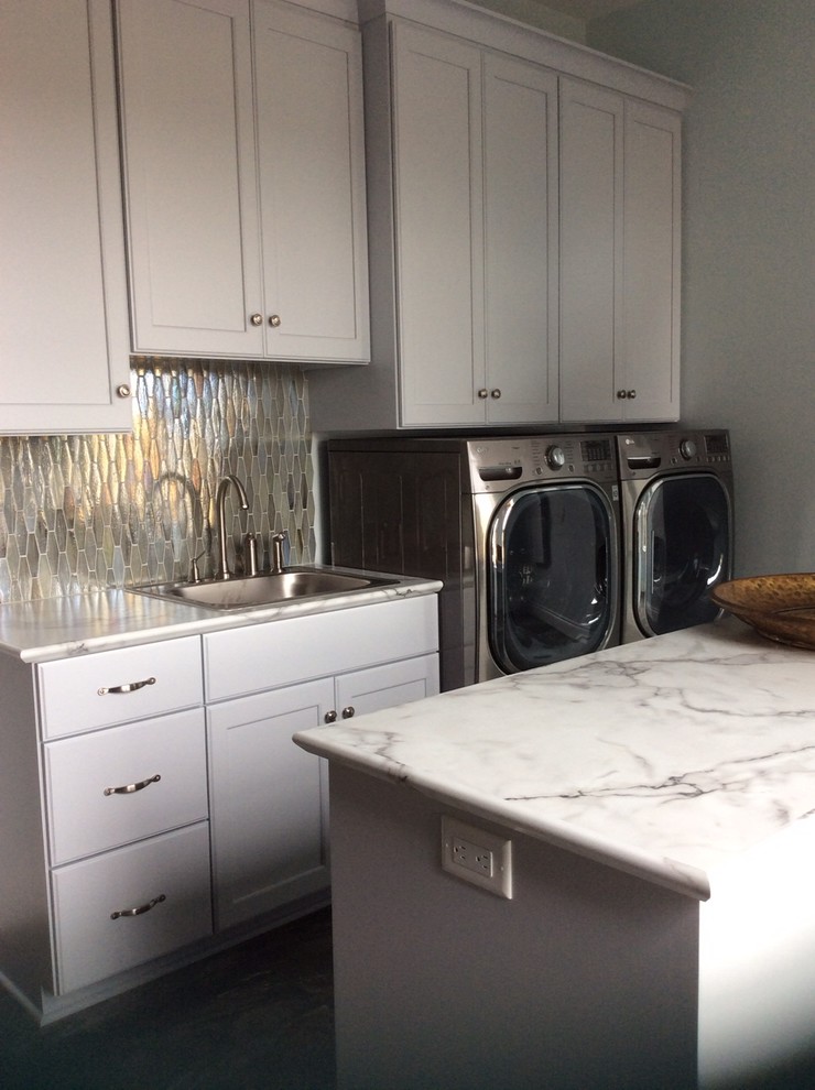 Photo of a mid-sized galley dedicated laundry room in Cleveland with a drop-in sink, recessed-panel cabinets, white cabinets, marble benchtops, grey walls and a side-by-side washer and dryer.