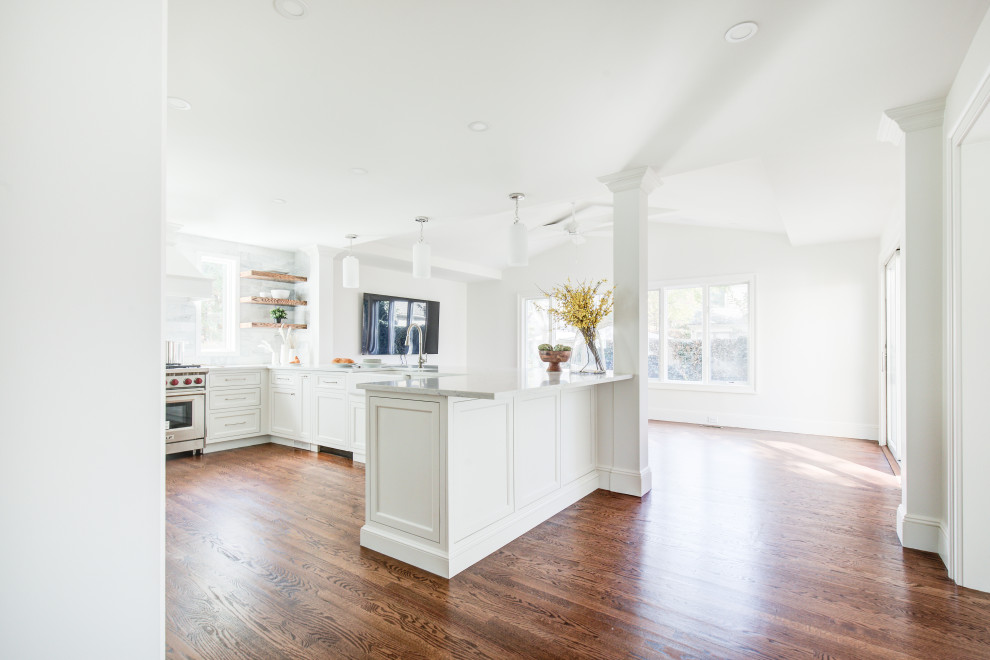 Open concept kitchen - mid-sized transitional u-shaped medium tone wood floor and brown floor open concept kitchen idea with a farmhouse sink, recessed-panel cabinets, white cabinets, quartz countertops, multicolored backsplash, marble backsplash, stainless steel appliances, a peninsula and white countertops