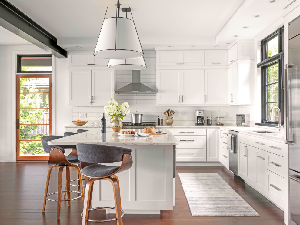 Inspiration for a transitional l-shaped kitchen in Burlington with an undermount sink, shaker cabinets, white cabinets, white splashback, stainless steel appliances, dark hardwood floors, with island, brown floor and white benchtop.