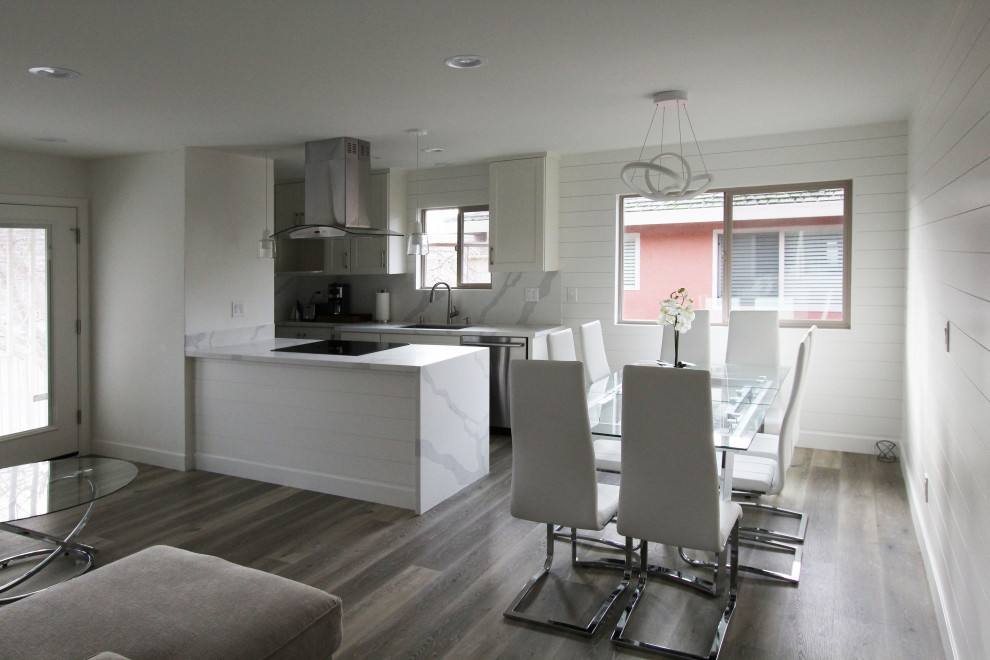 Open concept kitchen - small galley vinyl floor and brown floor open concept kitchen idea with an undermount sink, shaker cabinets, white cabinets, quartz countertops, white backsplash, quartz backsplash, stainless steel appliances, a peninsula and white countertops