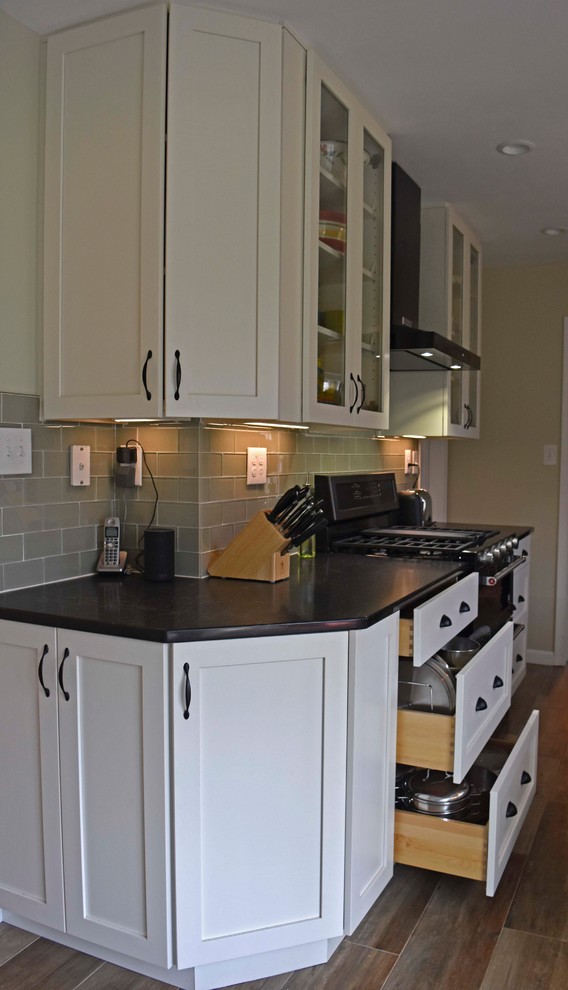 Enclosed kitchen - mid-sized transitional galley laminate floor and brown floor enclosed kitchen idea in DC Metro with a farmhouse sink, shaker cabinets, white cabinets, granite countertops, gray backsplash, subway tile backsplash, stainless steel appliances, no island and black countertops