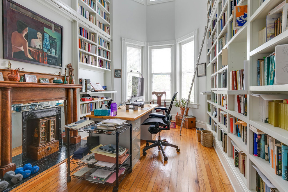 Imagen de despacho clásico de tamaño medio con biblioteca, paredes blancas, suelo de madera en tonos medios, todas las chimeneas, marco de chimenea de madera, escritorio independiente y suelo marrón