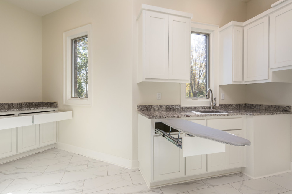 Photo of a large contemporary u-shaped utility room in Other with an undermount sink, shaker cabinets, white cabinets, granite benchtops, beige walls, marble floors, a side-by-side washer and dryer and white floor.