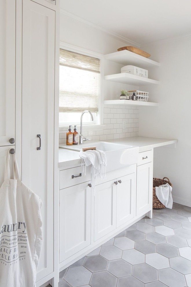 This is an example of a country laundry room in Houston with a farmhouse sink, shaker cabinets, white cabinets, white walls, grey floor and white benchtop.