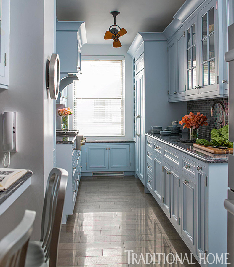 Photo of a small traditional galley kitchen in New York with an undermount sink, raised-panel cabinets, blue cabinets, granite benchtops, grey splashback, glass tile splashback, panelled appliances and porcelain floors.