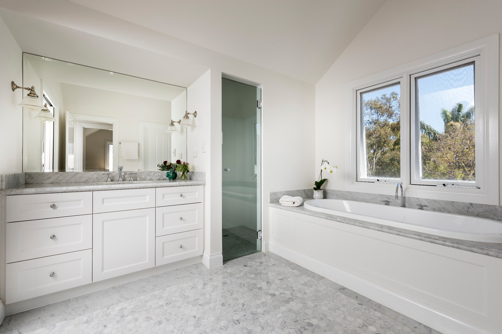 Inspiration for a mid-sized beach style master wet room bathroom in Perth with shaker cabinets, white cabinets, a drop-in tub, white walls, marble floors, an undermount sink, marble benchtops, grey floor and a hinged shower door.