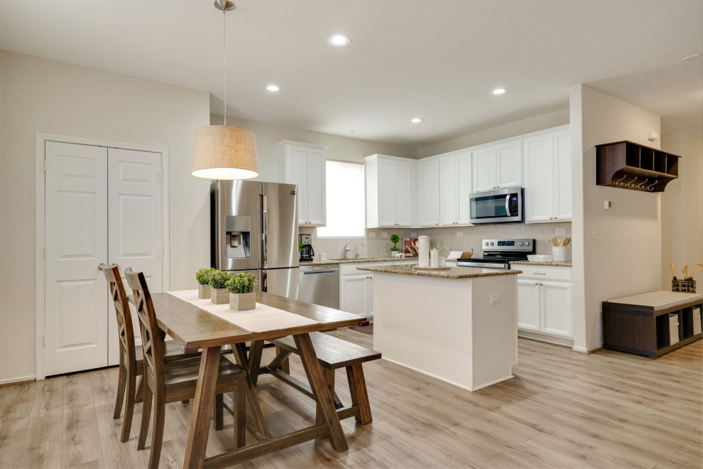 L-shaped laminate floor and brown floor eat-in kitchen photo with an undermount sink, white cabinets, granite countertops, beige backsplash, stainless steel appliances, an island and white countertops