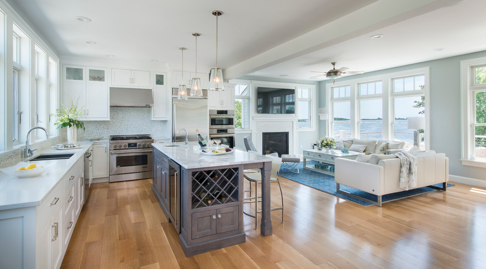 Inspiration for a mid-sized beach style u-shaped open plan kitchen in Providence with an undermount sink, shaker cabinets, grey cabinets, quartz benchtops, white splashback, stone tile splashback, stainless steel appliances, light hardwood floors and with island.