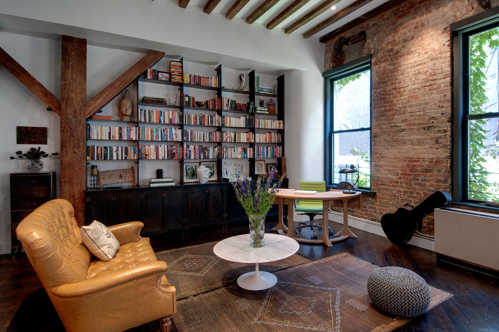 This is an example of an industrial family room in New York with a library, white walls, dark hardwood floors and no tv.