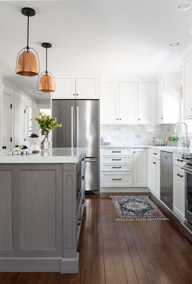 This is an example of a beach style l-shaped kitchen in Boston with an undermount sink, shaker cabinets, white cabinets, quartz benchtops, white splashback, marble splashback, stainless steel appliances, medium hardwood floors, brown floor and white benchtop.