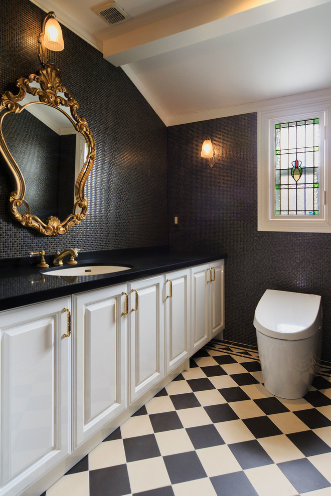 Inspiration for a large traditional powder room in Tokyo with raised-panel cabinets, white cabinets, a one-piece toilet, black tile, white tile, glass tile, black walls, ceramic floors, an undermount sink and black benchtops.