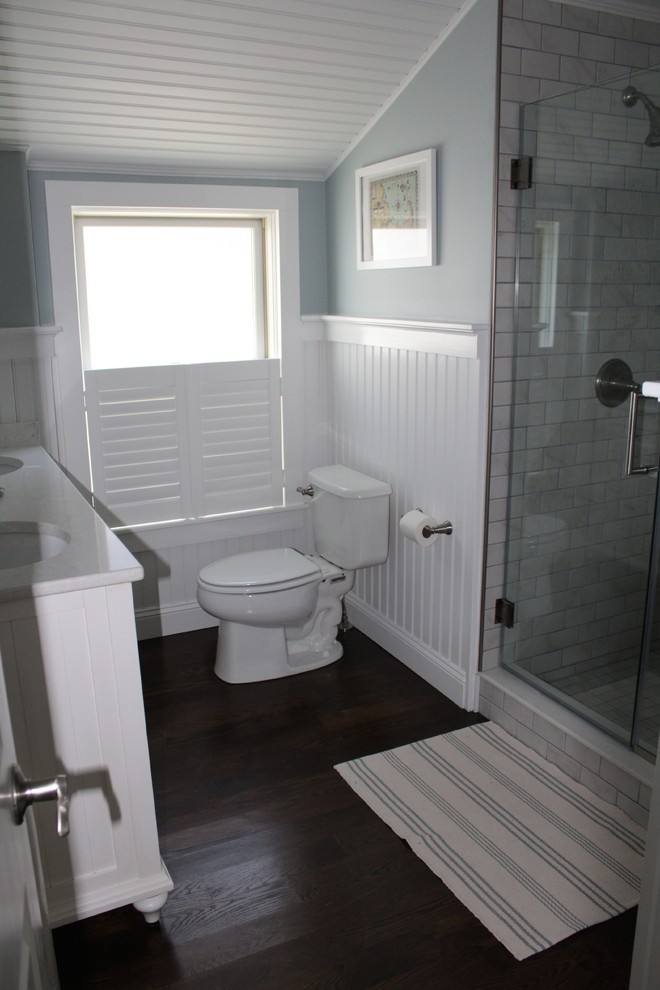 Photo of a mid-sized beach style master bathroom in Boston with beaded inset cabinets, white cabinets, a two-piece toilet, beige tile, blue walls, dark hardwood floors, an undermount sink, marble benchtops and an alcove shower.
