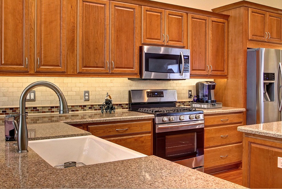 Eat-in kitchen - mid-sized l-shaped medium tone wood floor eat-in kitchen idea in Phoenix with a farmhouse sink, raised-panel cabinets, medium tone wood cabinets, beige backsplash, stone tile backsplash, stainless steel appliances and an island