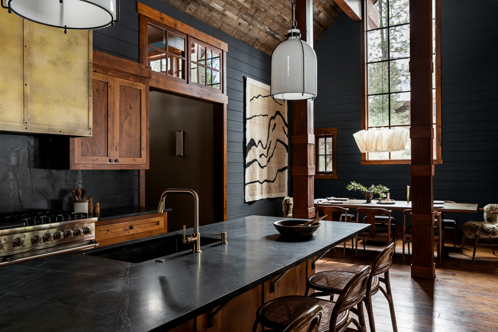 Inspiration for a large eclectic single-wall eat-in kitchen in Sacramento with an undermount sink, flat-panel cabinets, medium wood cabinets, soapstone benchtops, black splashback, stone slab splashback, stainless steel appliances, medium hardwood floors, with island, brown floor, black benchtop and wood.