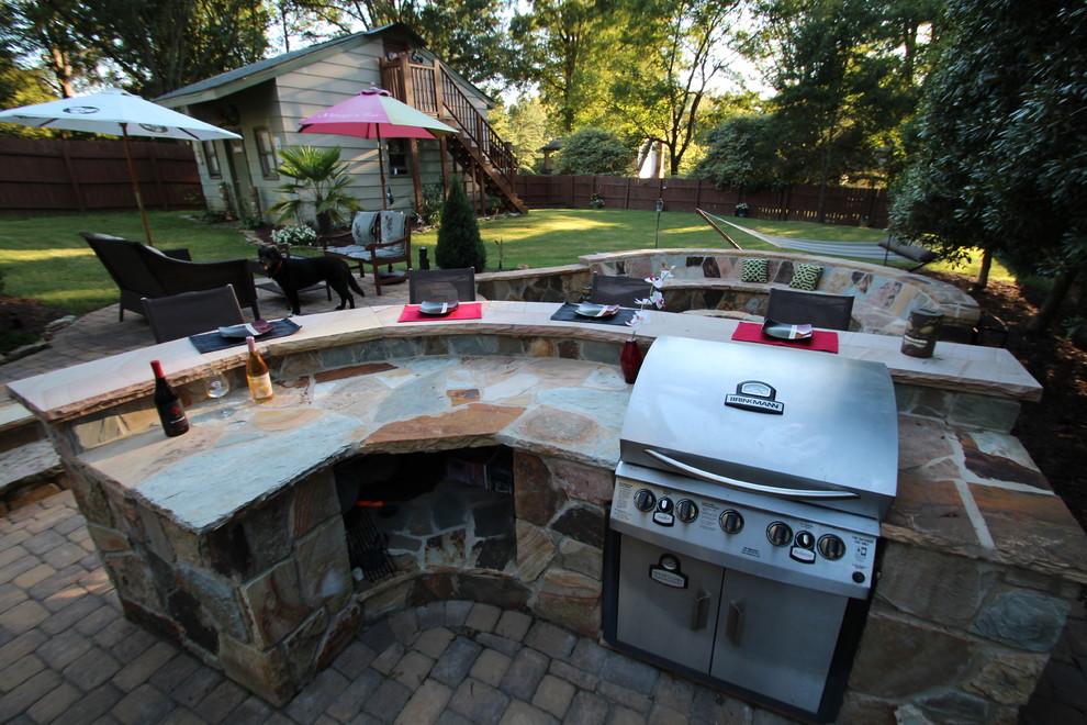 This is an example of a large contemporary backyard patio in Charlotte with an outdoor kitchen, natural stone pavers and no cover.