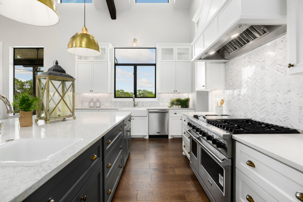 Mid-sized country u-shaped open plan kitchen in Austin with a farmhouse sink, recessed-panel cabinets, white cabinets, marble benchtops, white splashback, porcelain splashback, stainless steel appliances, dark hardwood floors, with island, brown floor, white benchtop and vaulted.