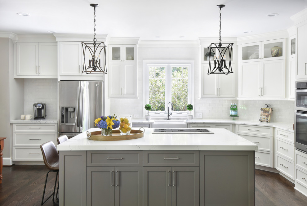 Inspiration for a large transitional l-shaped kitchen in Atlanta with a farmhouse sink, shaker cabinets, white cabinets, quartz benchtops, white splashback, stainless steel appliances, dark hardwood floors, with island, brown floor, white benchtop and subway tile splashback.