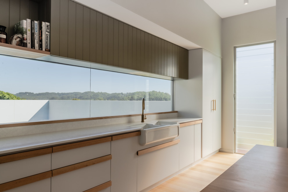 This is an example of a large u-shaped kitchen pantry in Sunshine Coast with a farmhouse sink, shaker cabinets, green cabinets, laminate benchtops, white splashback, black appliances, laminate floors, with island, beige floor and beige benchtop.