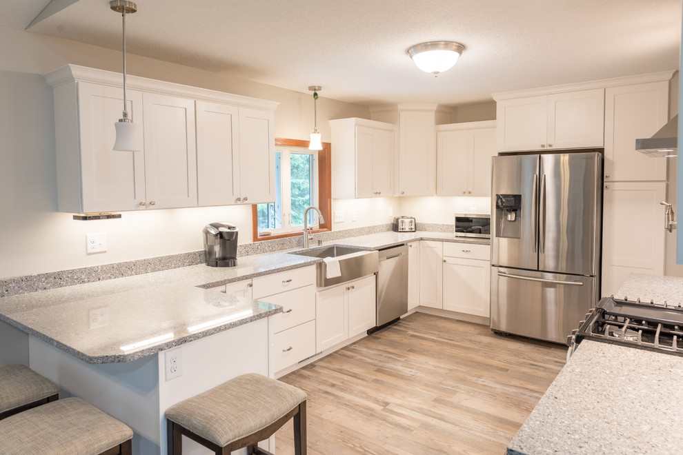 Example of a large transitional u-shaped light wood floor and brown floor enclosed kitchen design in Minneapolis with a farmhouse sink, shaker cabinets, white cabinets, granite countertops, stainless steel appliances, a peninsula and gray countertops