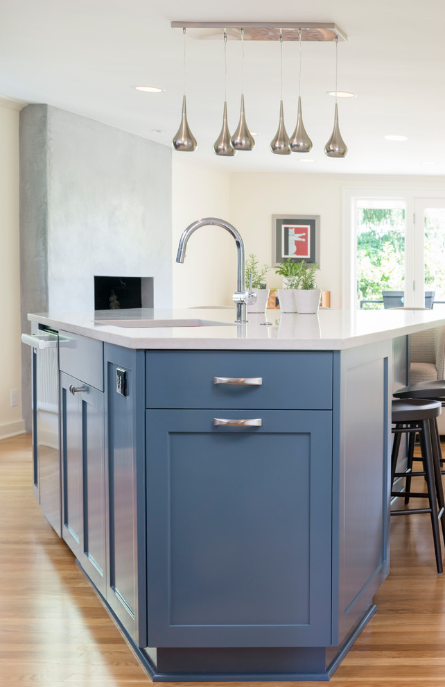 Mid-sized transitional l-shaped medium tone wood floor and brown floor open concept kitchen photo in Seattle with an undermount sink, shaker cabinets, blue cabinets, solid surface countertops, white backsplash, stone slab backsplash, stainless steel appliances, an island and white countertops