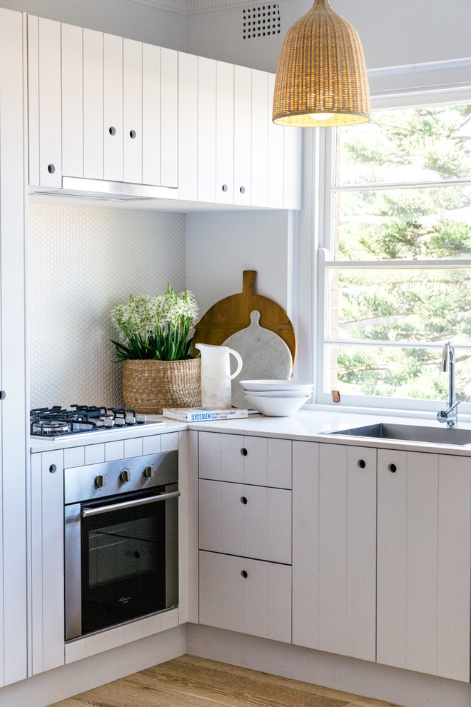 This is an example of a small beach style l-shaped kitchen in Sydney with white cabinets, white splashback, mosaic tile splashback and stainless steel appliances.