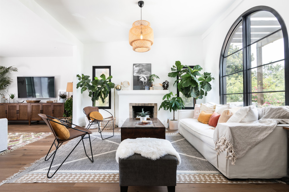 Inspiration for a mid-sized mediterranean open concept family room in Los Angeles with white walls, medium hardwood floors, a standard fireplace, a plaster fireplace surround, a wall-mounted tv, brown floor and vaulted.