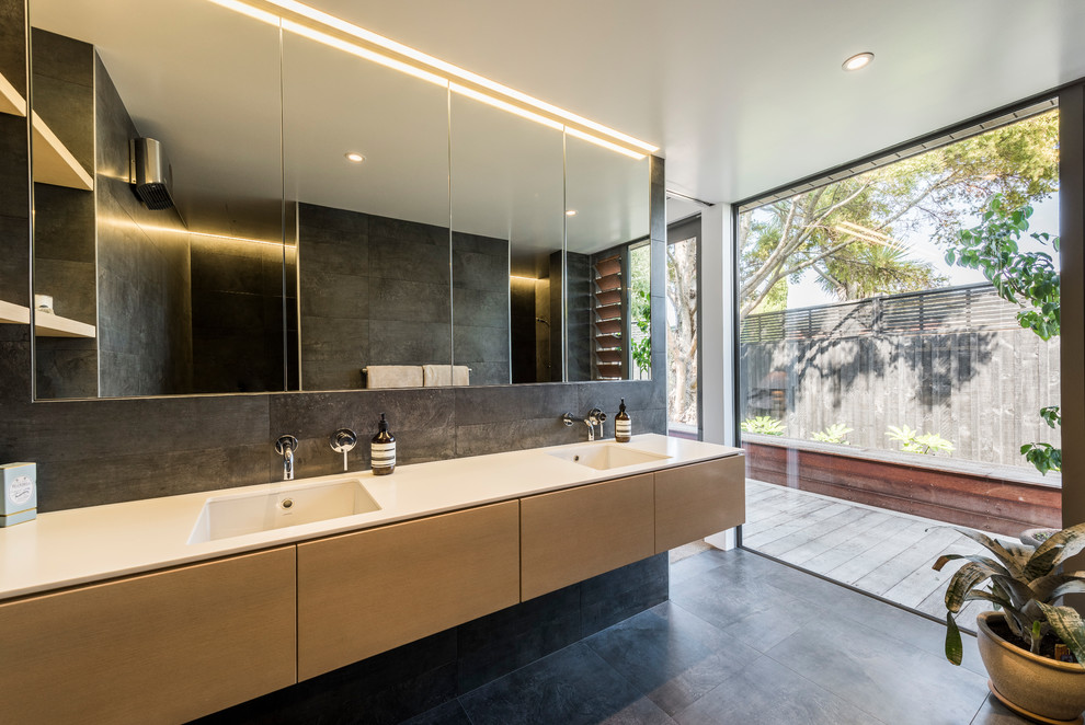 Large contemporary master bathroom in Christchurch with light wood cabinets, black tile, ceramic tile, flat-panel cabinets, an alcove shower, black walls, an integrated sink, black floor, an open shower and beige benchtops.