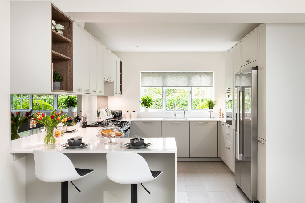 Photo of a contemporary kitchen in London with an undermount sink, shaker cabinets, grey cabinets, stainless steel appliances, a peninsula, grey floor and white benchtop.