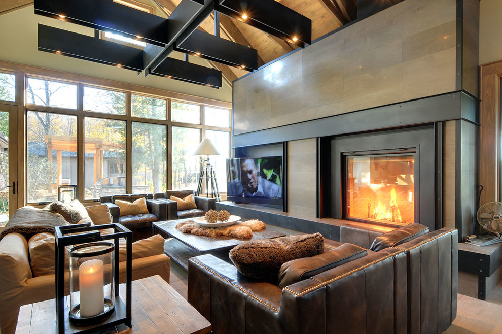 Photo of a mid-sized industrial formal enclosed living room in Toronto with beige walls, light hardwood floors, a standard fireplace, a metal fireplace surround, a wall-mounted tv and brown floor.