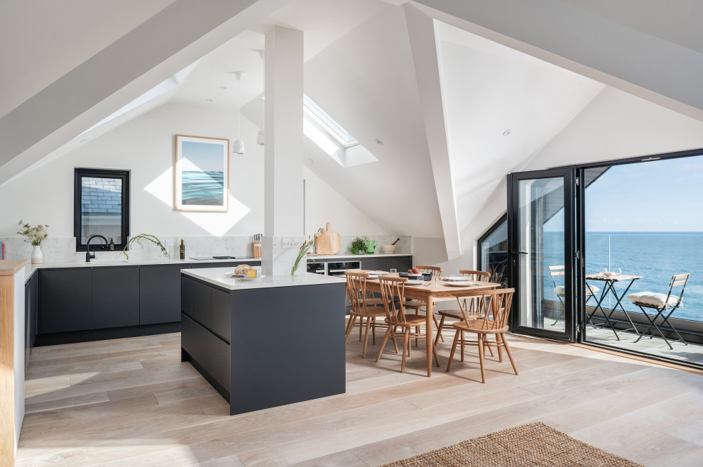 Medium sized coastal l-shaped open plan kitchen in Cornwall with a built-in sink, flat-panel cabinets, blue cabinets, quartz worktops, stainless steel appliances, light hardwood flooring, an island and white worktops.