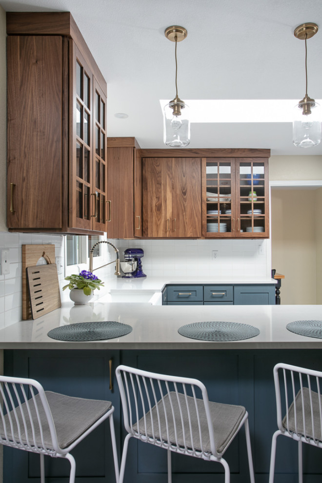 Mid-sized transitional u-shaped eat-in kitchen in Denver with a farmhouse sink, shaker cabinets, medium wood cabinets, quartz benchtops, white splashback, porcelain splashback, stainless steel appliances, porcelain floors, with island, multi-coloured floor and white benchtop.