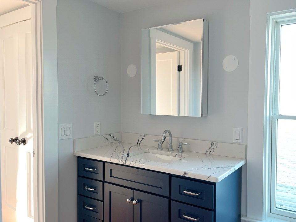 This is an example of a small beach style 3/4 bathroom in Providence with shaker cabinets, blue cabinets, an alcove shower, a two-piece toilet, white tile, grey walls, medium hardwood floors, an undermount sink, engineered quartz benchtops, a hinged shower door, white benchtops, a single vanity and a freestanding vanity.