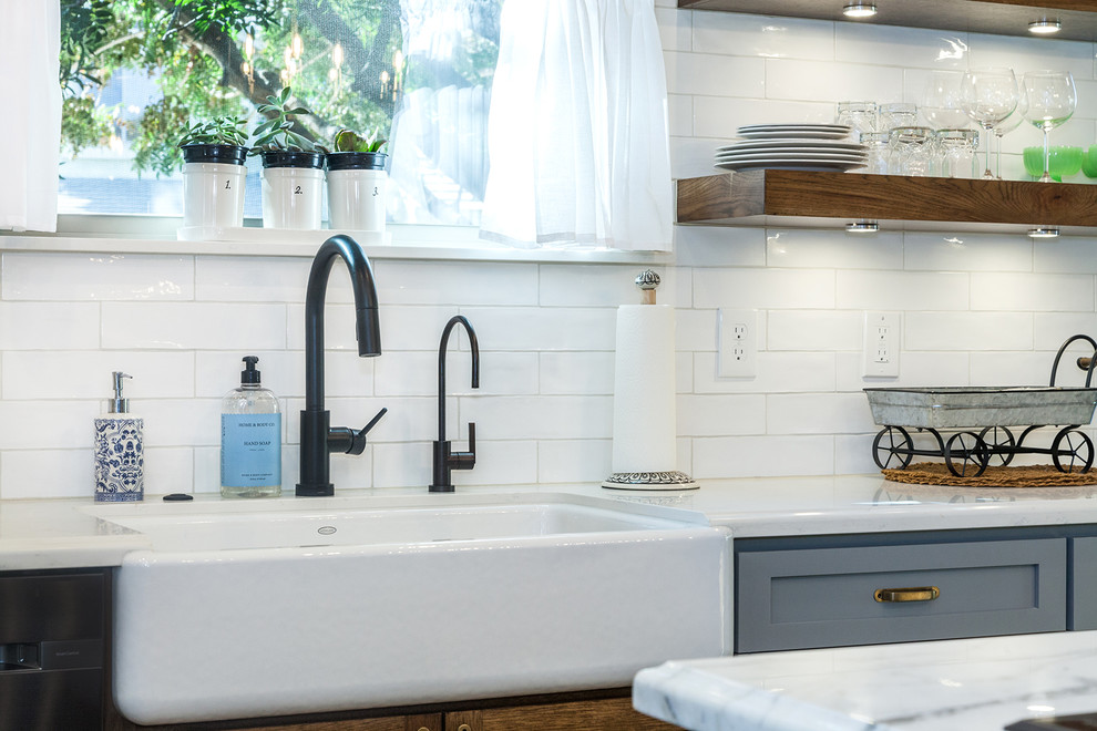 Example of a large transitional l-shaped porcelain tile and brown floor eat-in kitchen design in Phoenix with a farmhouse sink, shaker cabinets, gray cabinets, quartz countertops, white backsplash, glass sheet backsplash, stainless steel appliances, an island and white countertops
