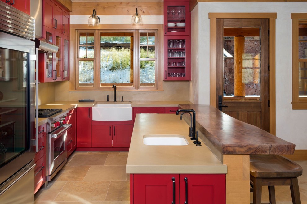 Inspiration for a mid-sized rustic u-shaped limestone floor and beige floor open concept kitchen remodel in Denver with a farmhouse sink, red cabinets, beige backsplash, stone slab backsplash, stainless steel appliances, a peninsula, glass-front cabinets and quartz countertops