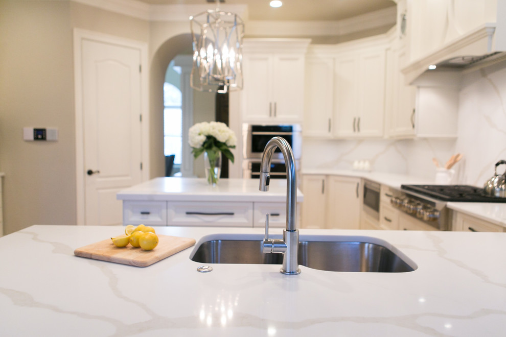Open concept kitchen - mid-sized transitional u-shaped open concept kitchen idea in Orlando with an undermount sink, recessed-panel cabinets, white cabinets, quartzite countertops, white backsplash, stone slab backsplash, stainless steel appliances and a peninsula