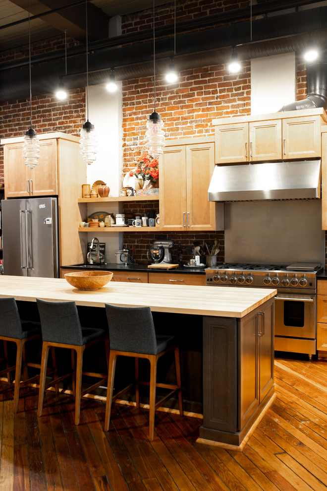 This is an example of a mid-sized transitional single-wall eat-in kitchen in Charlotte with an undermount sink, recessed-panel cabinets, medium wood cabinets, soapstone benchtops, red splashback, brick splashback, stainless steel appliances, medium hardwood floors, with island, brown floor and black benchtop.
