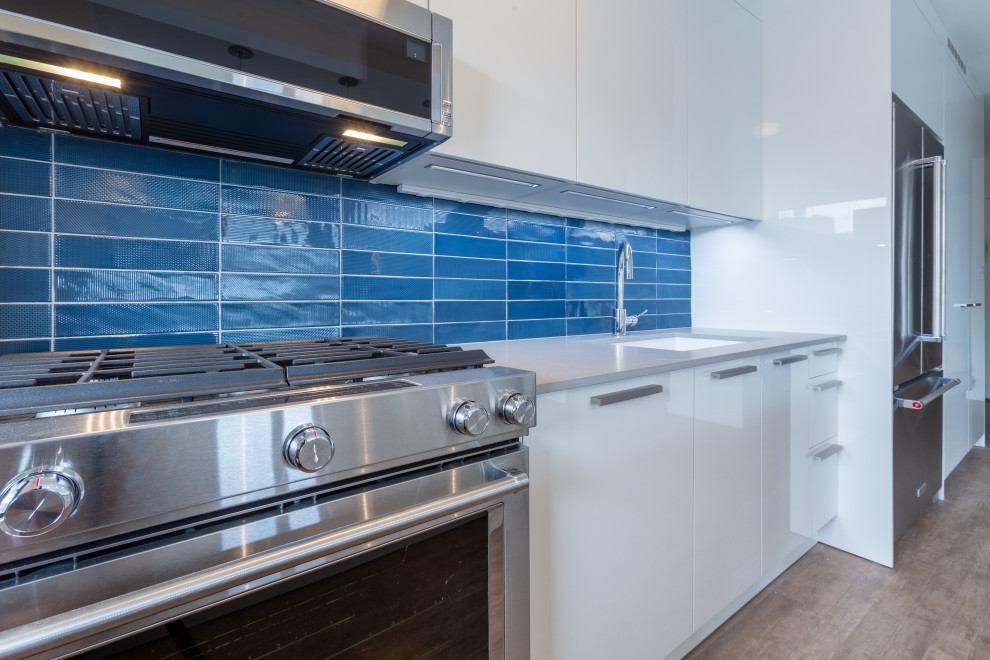 Mid-sized modern galley eat-in kitchen in New York with an undermount sink, flat-panel cabinets, white cabinets, quartz benchtops, blue splashback, ceramic splashback, panelled appliances, painted wood floors, with island, beige floor and grey benchtop.