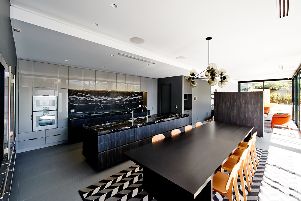 Design ideas for a large contemporary galley eat-in kitchen in Melbourne with an undermount sink, flat-panel cabinets, grey cabinets, marble benchtops, black splashback, stone slab splashback, porcelain floors, with island, stainless steel appliances and black benchtop.