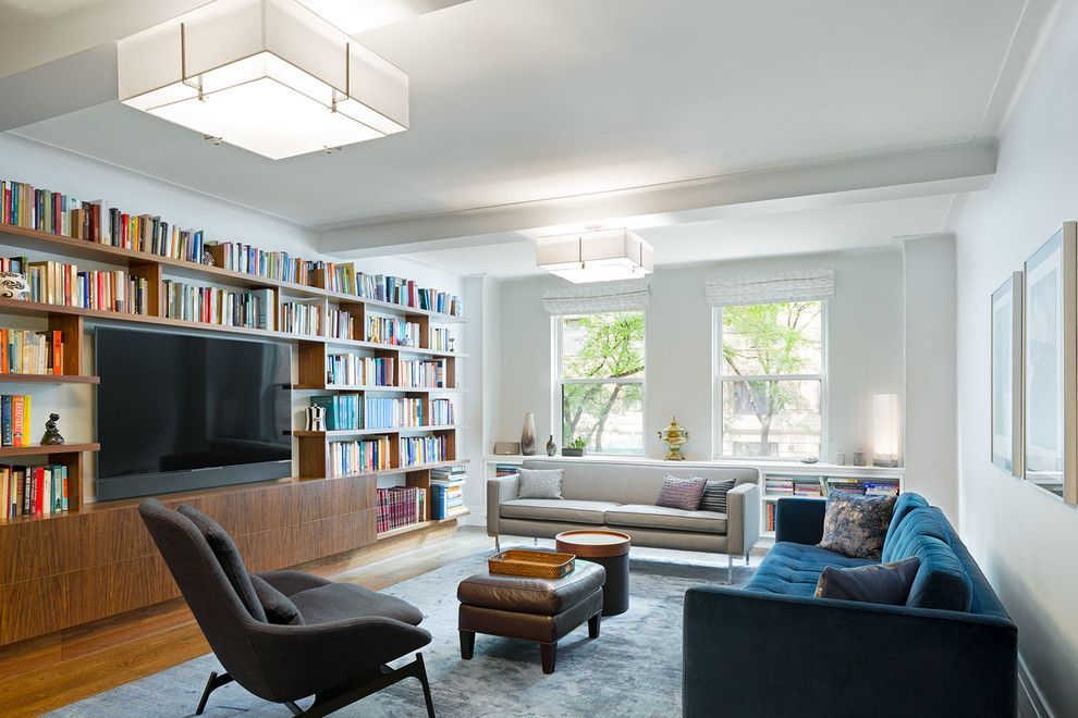 Inspiration for a large contemporary enclosed living room in New York with white walls, medium hardwood floors, a wall-mounted tv, a library and no fireplace.