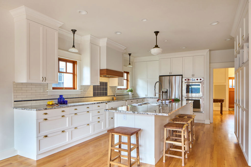 Inspiration for a mid-sized transitional medium tone wood floor and brown floor kitchen pantry remodel in Portland with an undermount sink, recessed-panel cabinets, white cabinets, granite countertops, white backsplash, ceramic backsplash, stainless steel appliances, an island and multicolored countertops