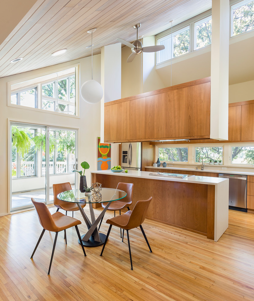Design ideas for a mid-sized midcentury eat-in kitchen in Minneapolis with flat-panel cabinets, solid surface benchtops, stainless steel appliances, light hardwood floors, with island, white benchtop and medium wood cabinets.