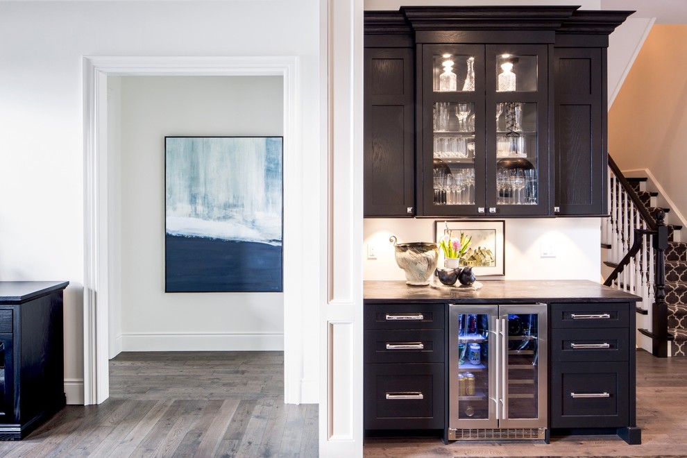 Mid-sized transitional single-wall medium tone wood floor and brown floor wet bar photo with no sink, shaker cabinets, dark wood cabinets, granite countertops and white backsplash