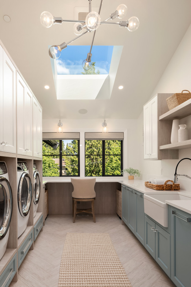 Design ideas for an expansive transitional u-shaped laundry room in Seattle with a farmhouse sink, recessed-panel cabinets, light wood cabinets, quartz benchtops, white walls, porcelain floors, a side-by-side washer and dryer and grey floor.